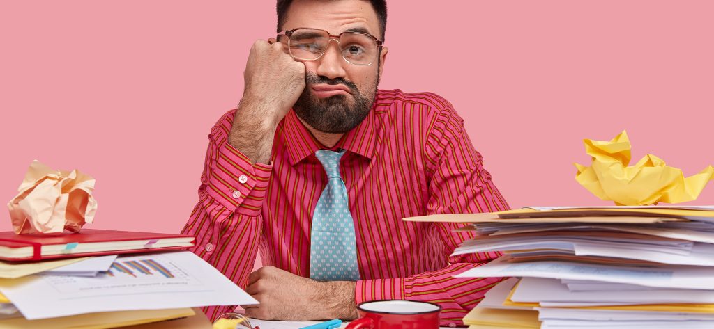 Homme débordé par le travail avec des piles de documents sur son bureau.