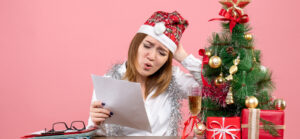 Personne stressée devant des dossiers et une mini déco de Noël, illustrant la surcharge administrative avant les congés de fin d’année.