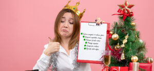 Femme souriante avec couronne et guirlande, tenant une checklist administrative devant un sapin de Noël, illustrant une organisation réussie en début d’année.