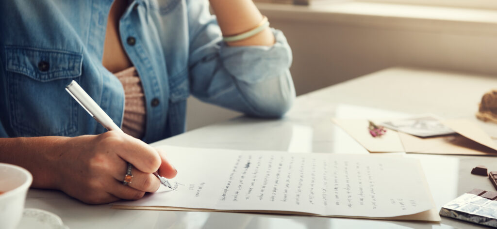 Personne rédigeant un courrier manuscrit à une table.